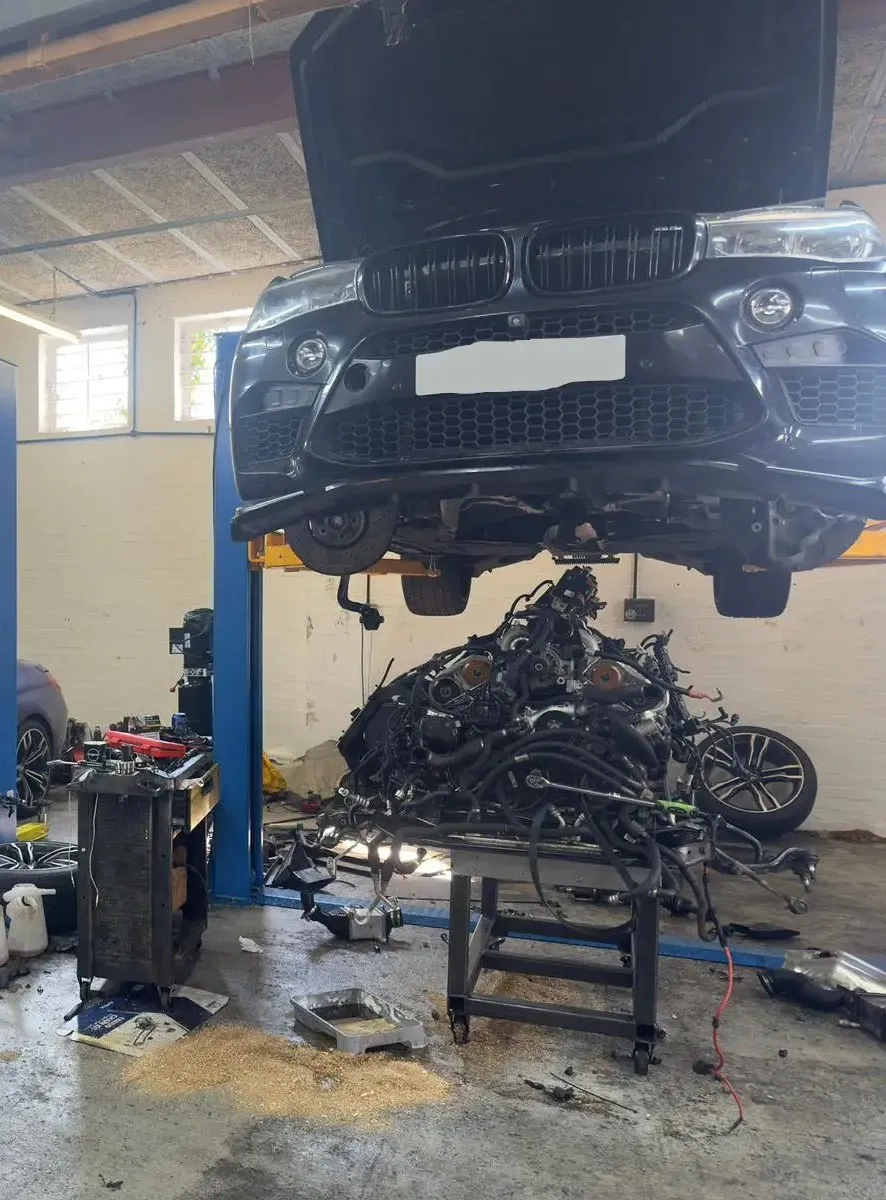 Blue BMW M6 and black BMW X5 in workshop with engines removed for rebuild at JLR Engine Specialists – IMI-certified technicians servicing high-performance BMW models