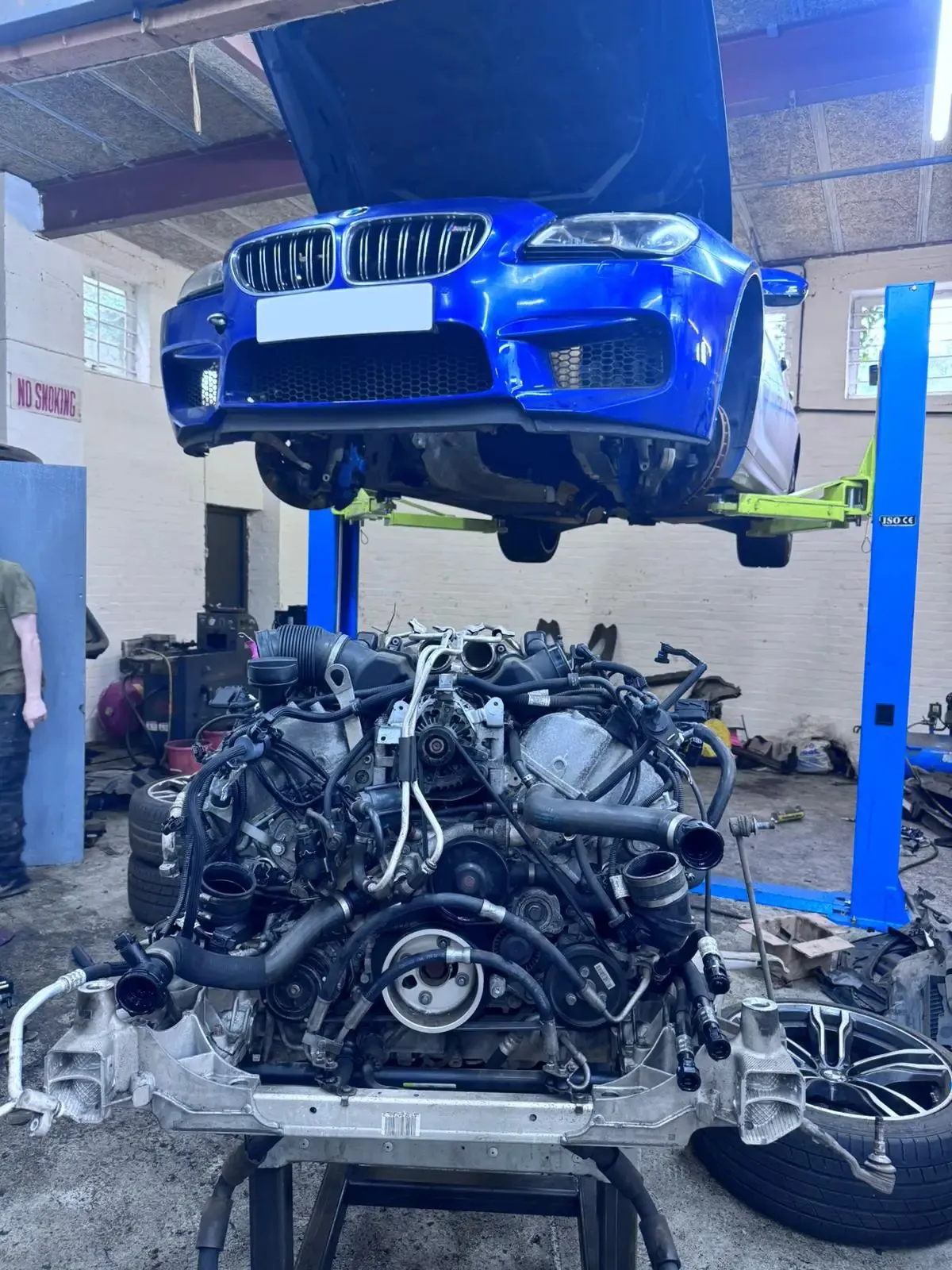 Blue BMW M5 on lift with engine removed for full rebuild at JLR Engine Specialists – IMI-certified technicians servicing high-performance BMW models using OEM-spec parts
