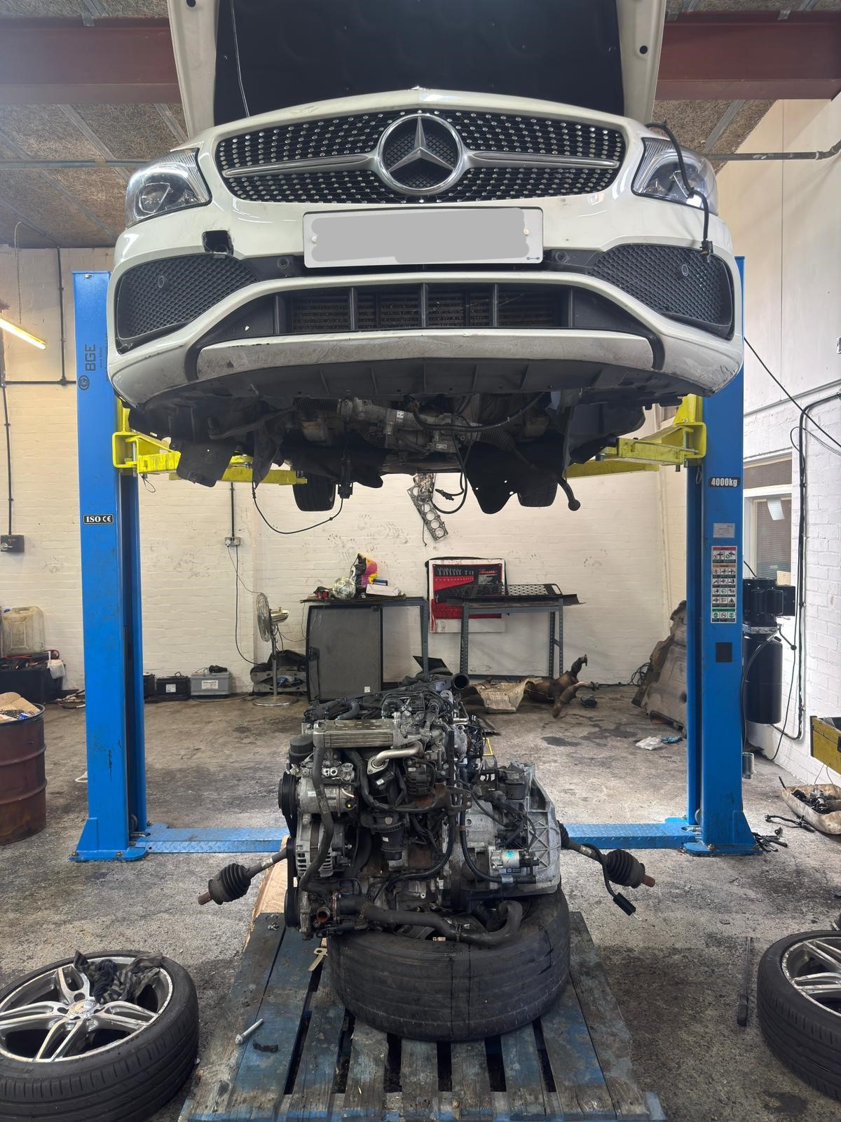 White Mercedes-Benz GLA on lift with engine removed for replacement at JLR Engine Specialists – IMI-certified technicians servicing luxury vehicles including BMW, Jaguar & Mercedes